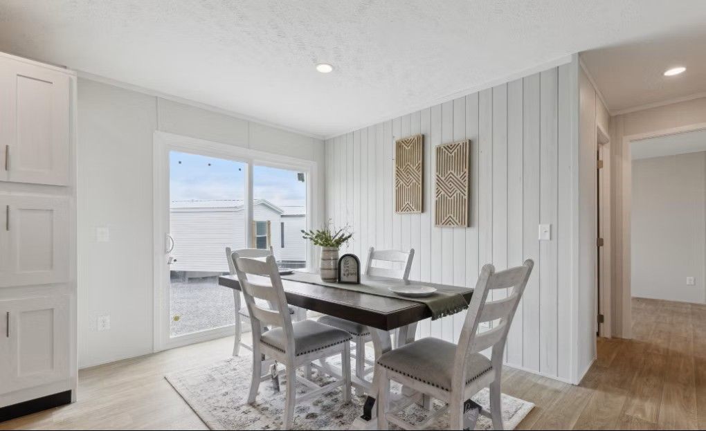 Dining room with white paneling, table, chairs, sliding glass door, and two wall art pieces.