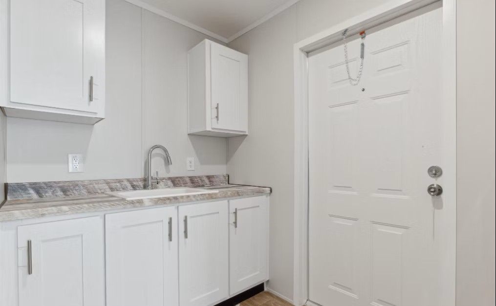 White kitchen cabinets and sink, with a white door on the right.