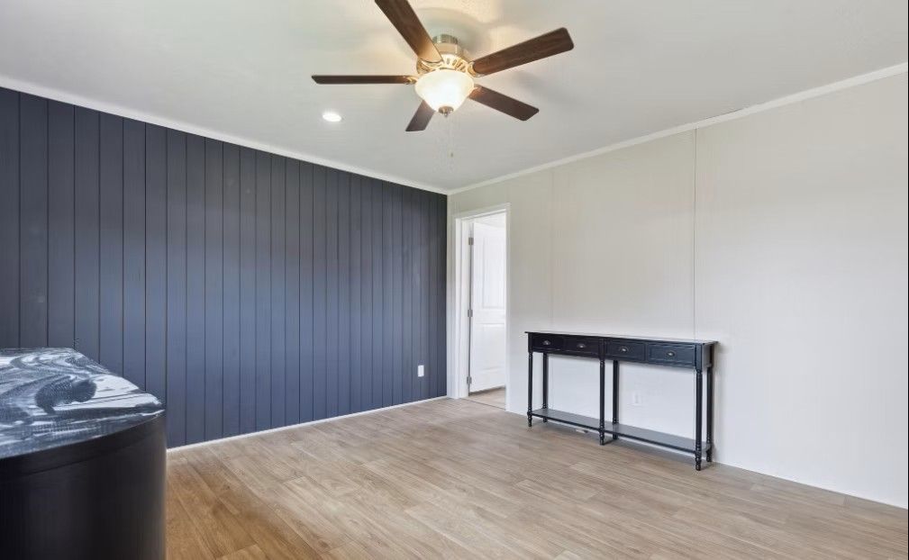 Empty room with blue wainscoting, white walls, wood-look floor, black table, ceiling fan, and open doorway.