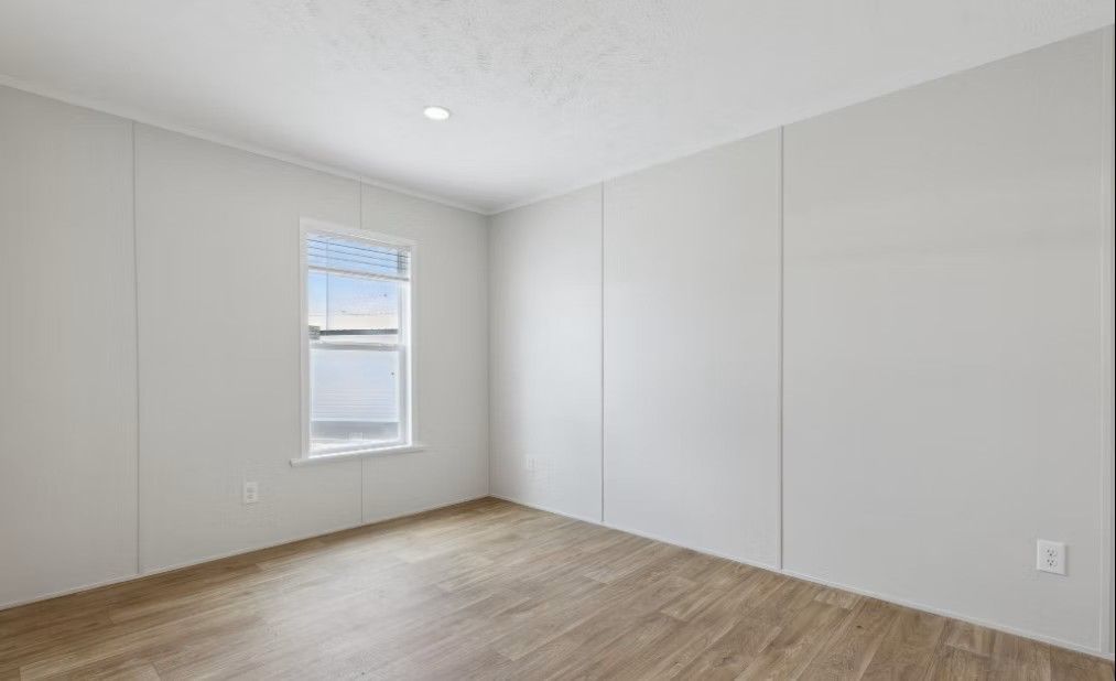 Empty room with light wood floors, white walls, small window, and a single light.