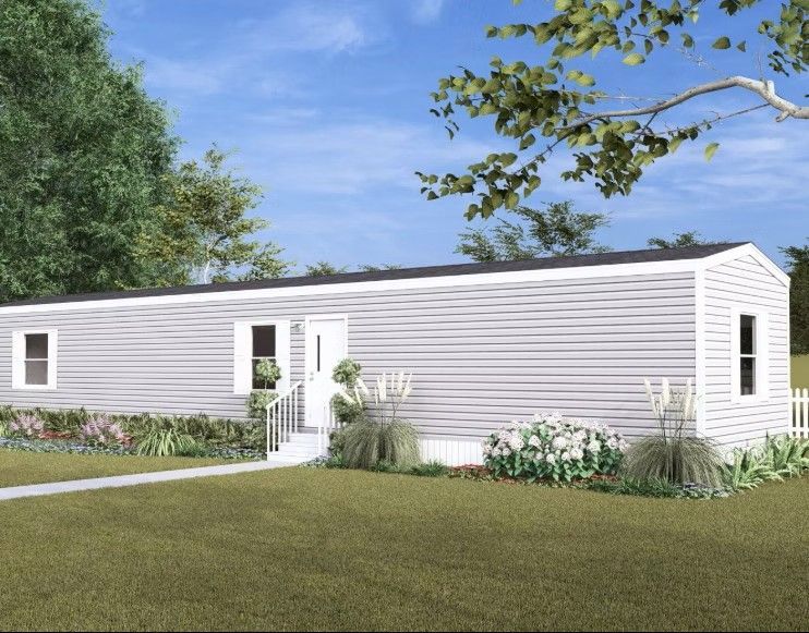 Single-story, light gray mobile home with white trim, set on a green lawn, under a blue sky.