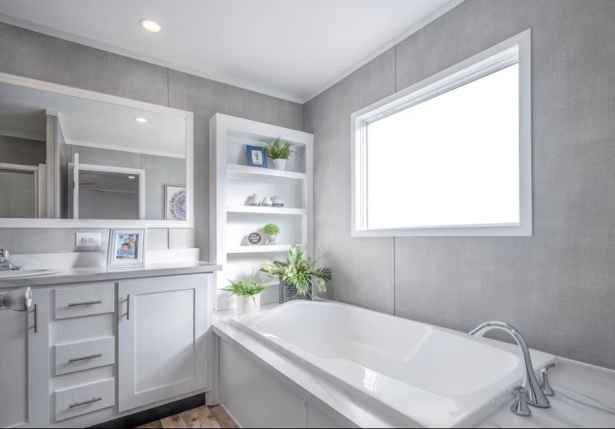 Bathroom with white tub, vanity, shelves, and window, gray walls and trim.