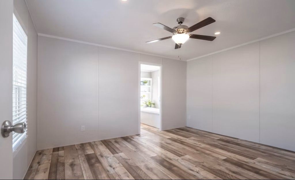 Empty room with light wood floor, white walls, ceiling fan, and window.