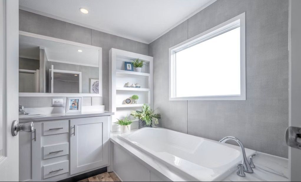 White bathroom with a tub, vanity, and a window. Gray walls and white cabinetry.