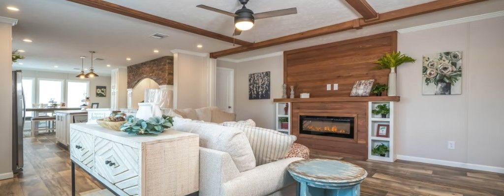 Living room with fireplace, white sofa, and wooden beams. Open to kitchen with island.