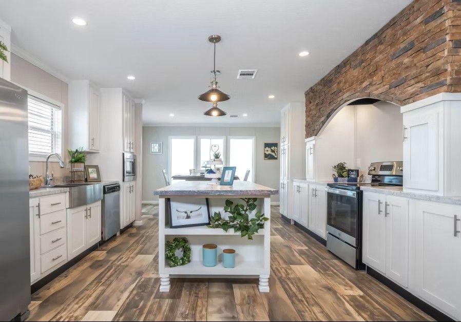 Bright white kitchen with island, wood flooring, stainless steel appliances, and brick wall accent.