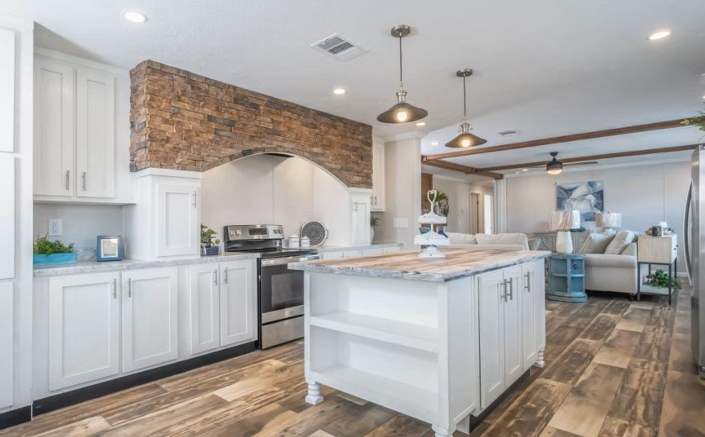 White kitchen with island, brick accent wall, stainless steel appliances, and wood-look flooring.