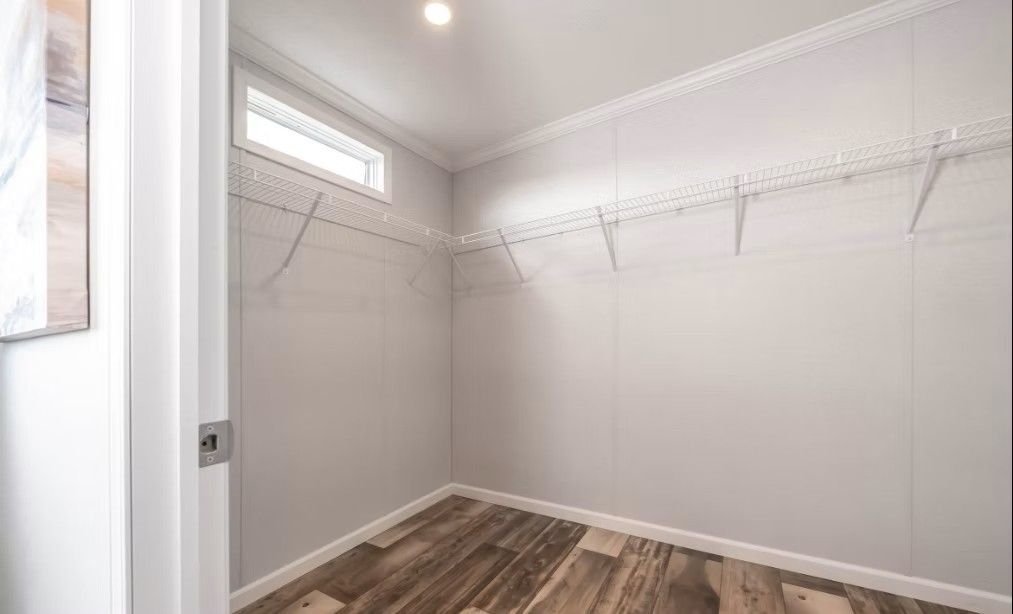 Empty walk-in closet with wire shelving and a small window. Wooden floor and white walls.