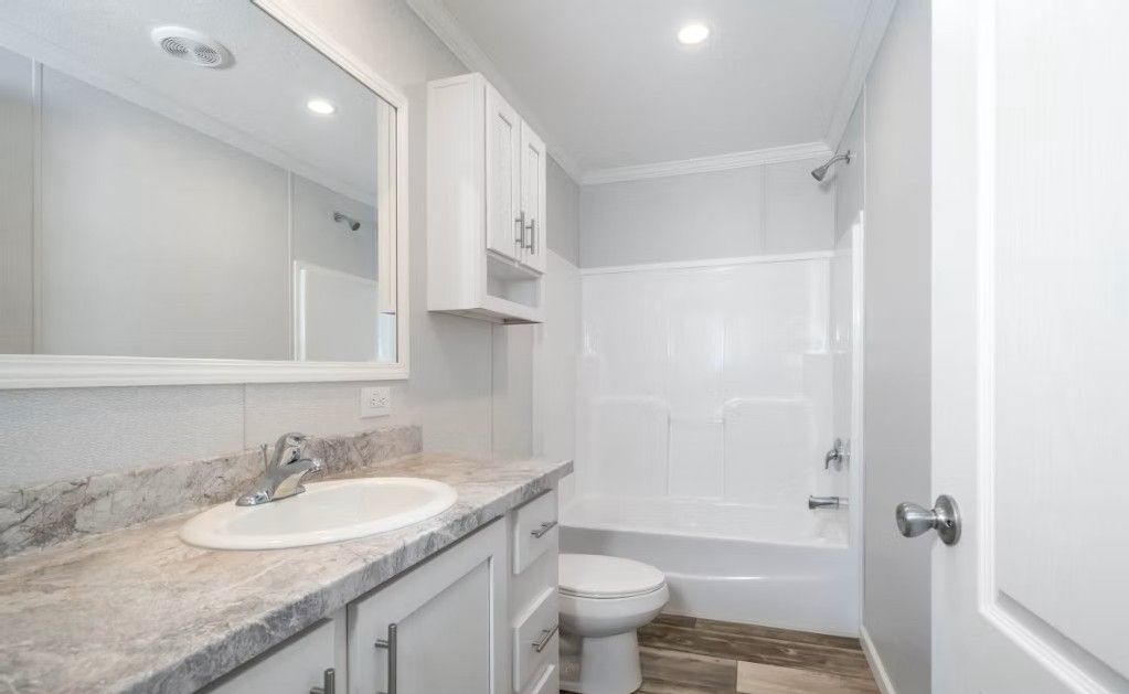 Bright white bathroom with vanity, toilet, shower, and cabinets.