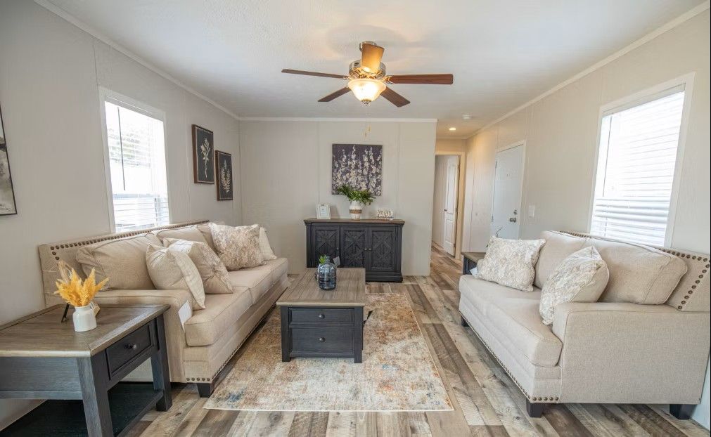 Living room with beige couches, dark furniture, hardwood floor, and a ceiling fan.