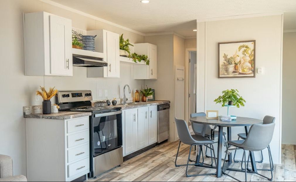 Kitchen with white cabinets, stainless steel appliances, plants, and a small dining table.