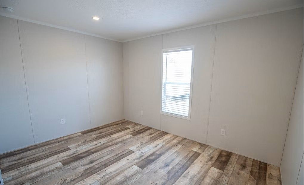 Empty room with light gray walls, wood-look flooring, and a small window.