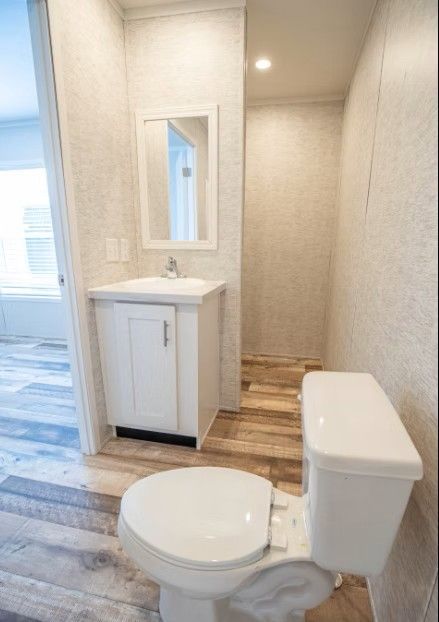 Small bathroom with a white toilet, sink, and mirror. Light wood-look flooring and textured walls.