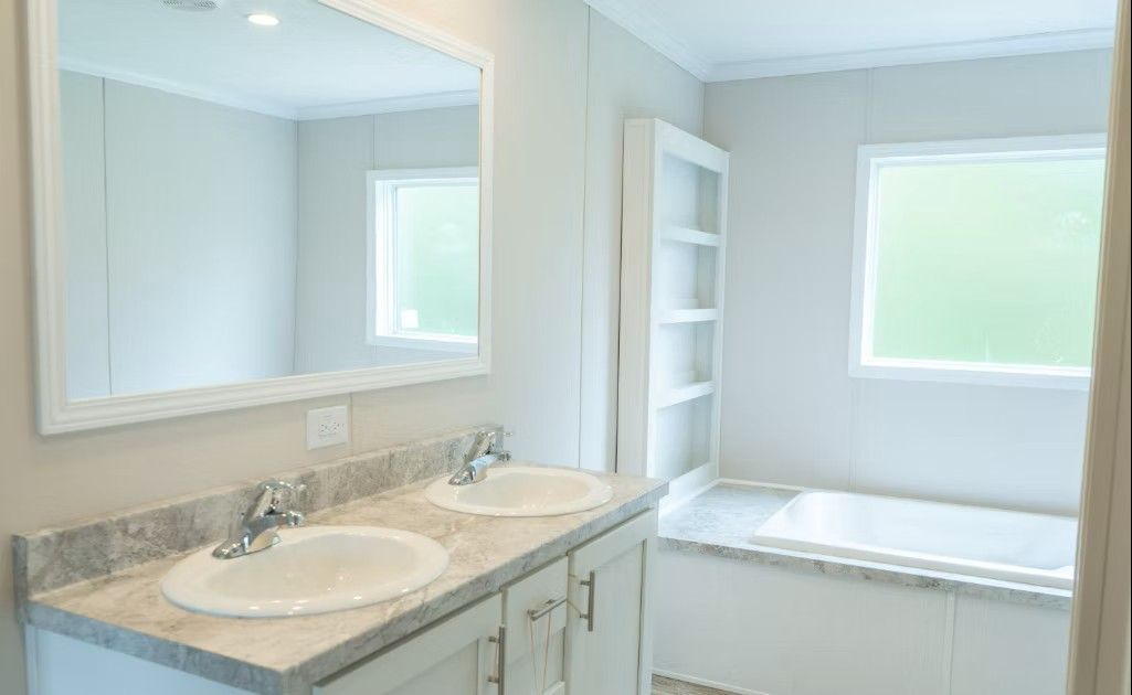 Bathroom with double sink vanity, built-in shelves, and a bathtub beneath a window.