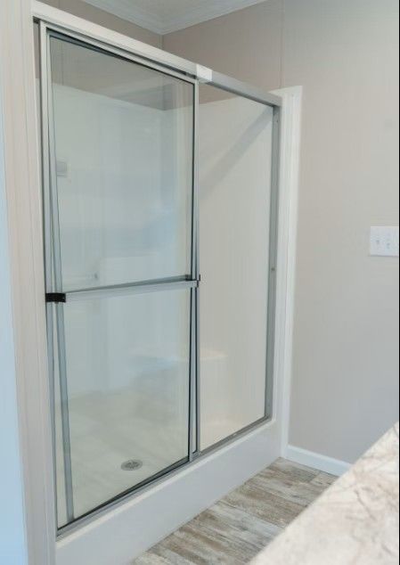 Shower stall with sliding glass doors; white walls, silver frame, light-colored flooring.