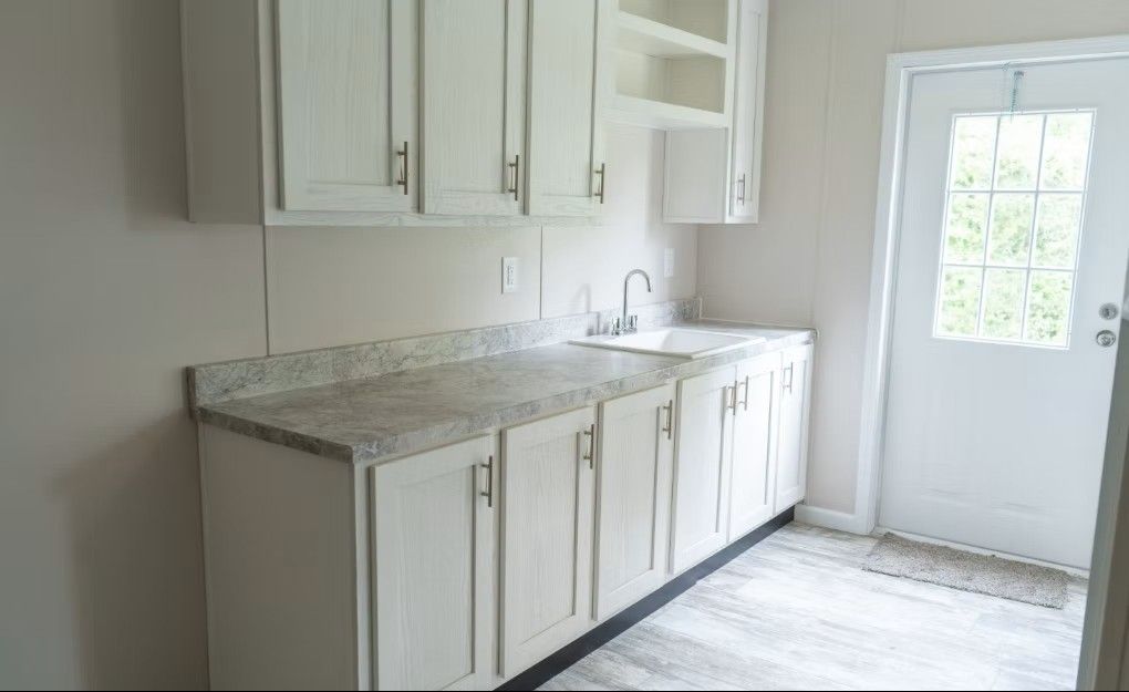 White kitchen cabinets and countertop, sink, and door to outside.