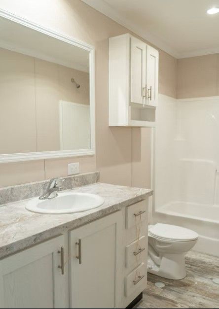 Bathroom with white cabinets, light countertop, large mirror, and tub/shower.