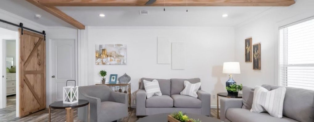 A bright living room with gray furniture and white walls. A barn door is on the left.