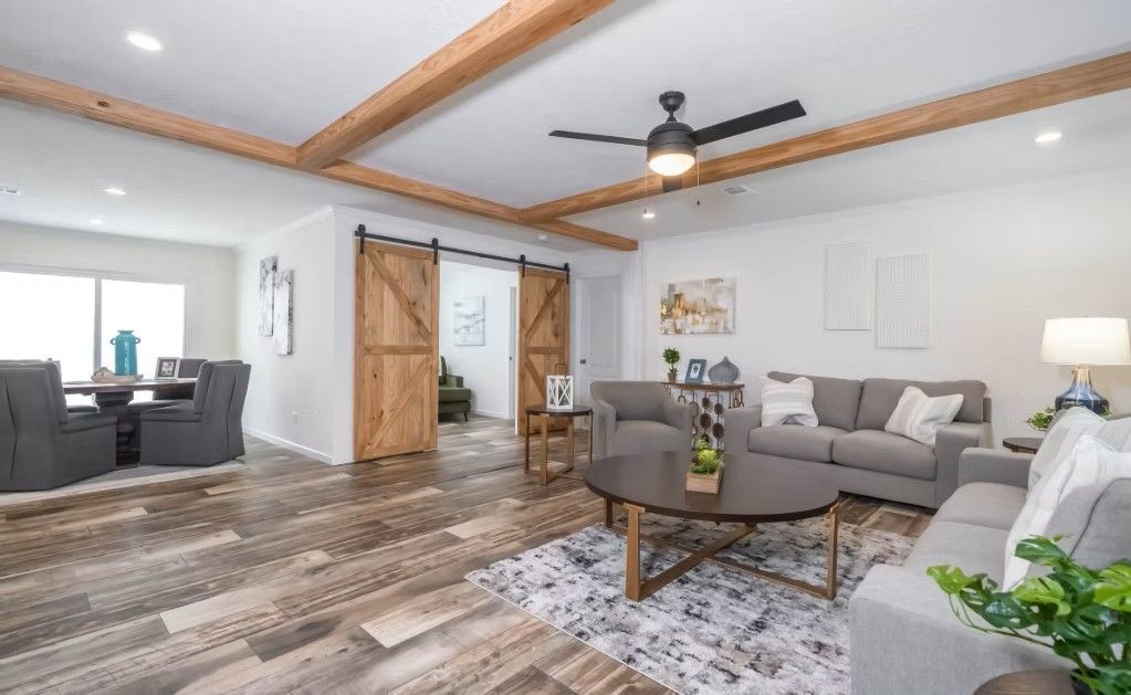 Spacious living room with wooden beams, barn doors, gray sofa, round coffee table, and area rug.