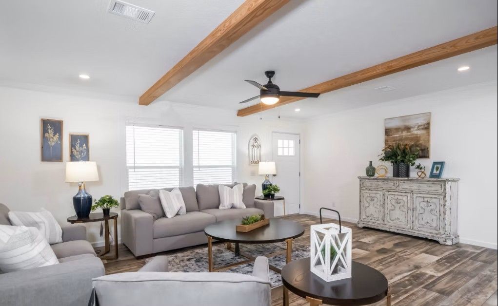 Spacious living room with gray furniture, wooden beams, and white walls.