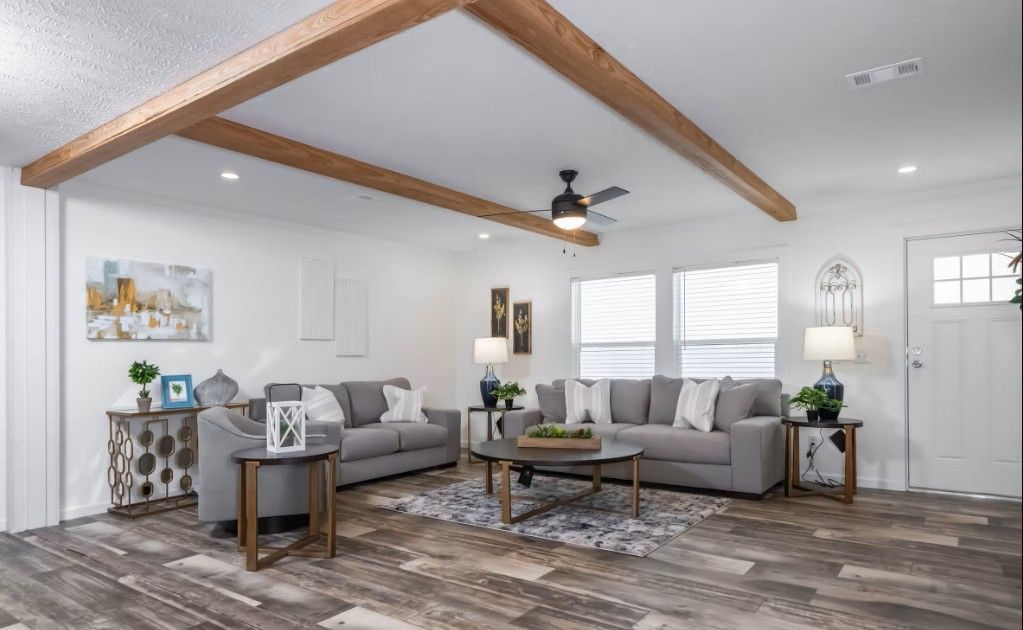 Spacious living room with gray sofas, wooden beams, hardwood floor, and natural light.
