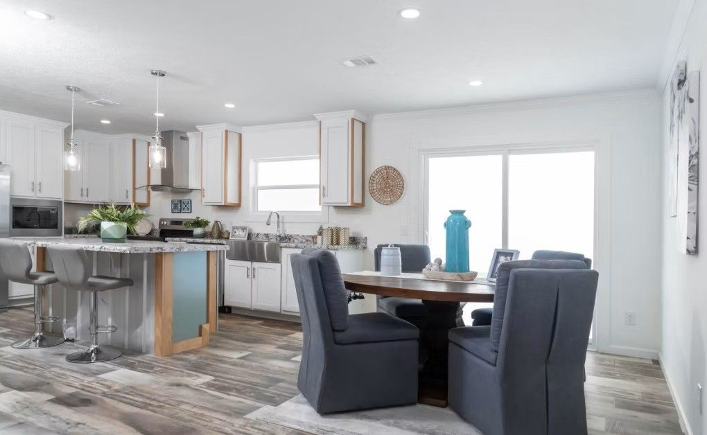 Open-concept kitchen and dining area with white cabinets, gray chairs, wooden table, and sliding glass door.