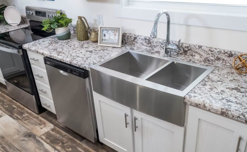 Kitchen with stainless steel sink, dishwasher, and stove, white cabinets, and granite countertop.