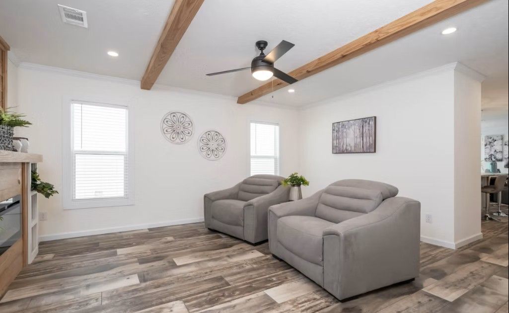 Living room with two gray armchairs, white walls, wood beams, and plank flooring.