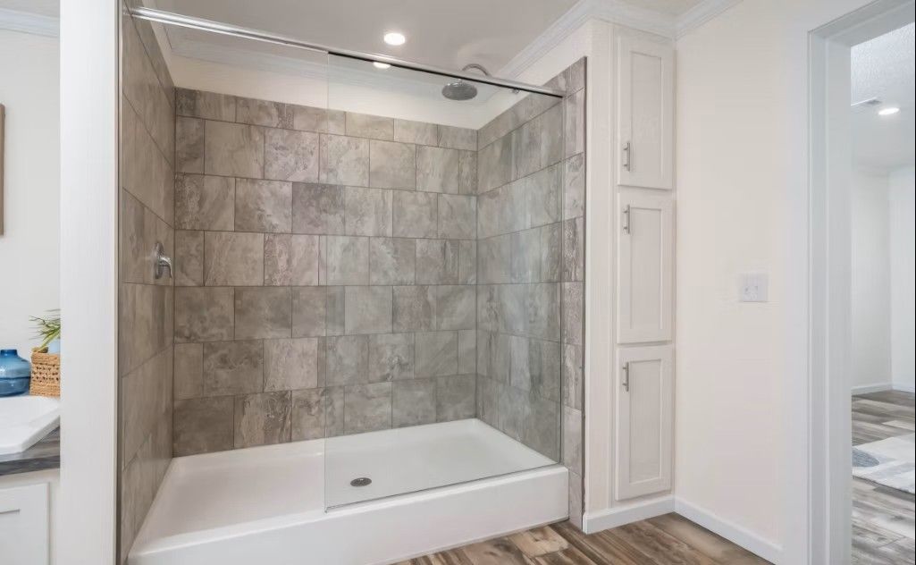 Bathroom with tiled shower, glass door, white base, and built-in cabinet.