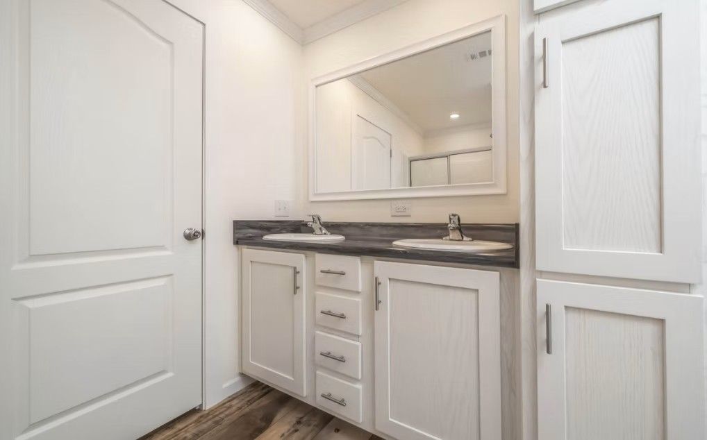 Bathroom with white cabinets, dark countertop, double sinks, and large mirror.