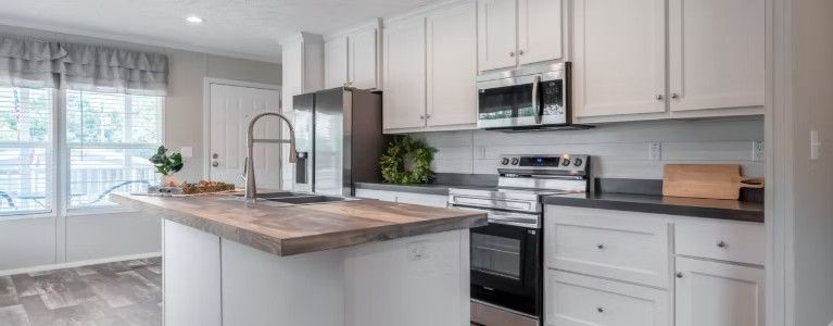 A modern kitchen with white cabinets, a wooden island, and stainless steel appliances.