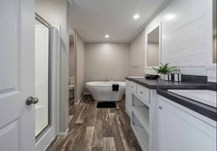 Bathroom with a white soaking tub, shower, vanity, and wood-look flooring.