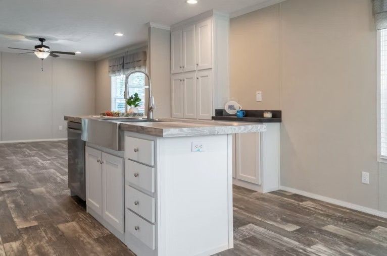Kitchen with white cabinets, gray countertops, and wood-look flooring. Island with sink.