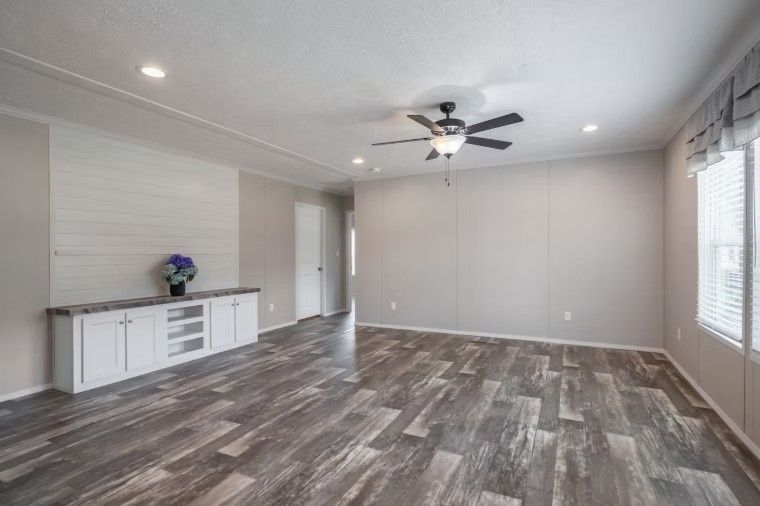 Empty living room with gray wood-look flooring, light gray walls, and white cabinet with floral arrangement.