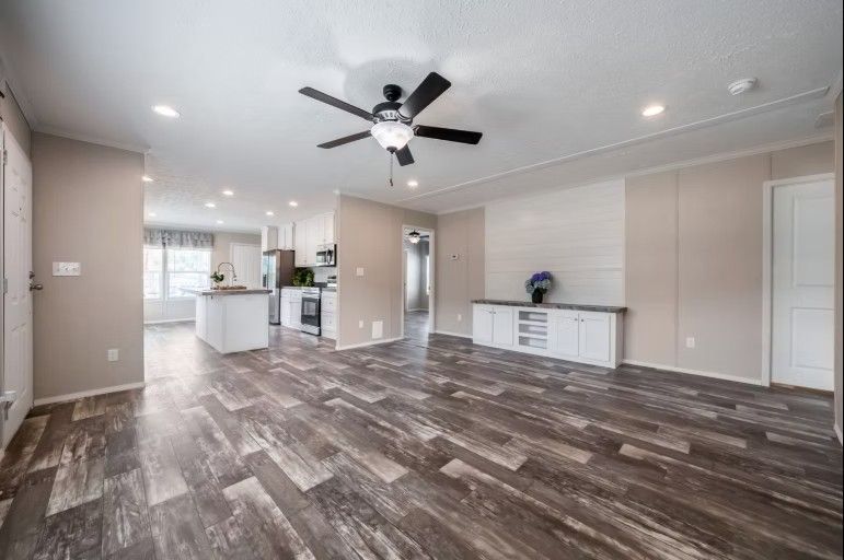 Spacious open-concept living area with dark wood-look flooring, white cabinets, and a black ceiling fan.