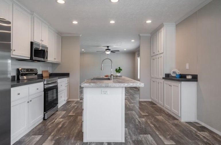 Kitchen with white cabinets, dark countertops, gray island, and wood-look flooring.