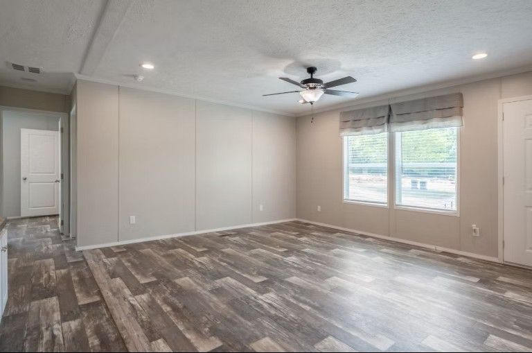 Empty room with wood-look floor, windows with shades, ceiling fan, and white walls.