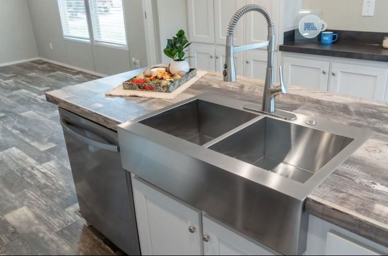 Stainless steel kitchen sink in a modern kitchen with a gray countertop and cabinets.