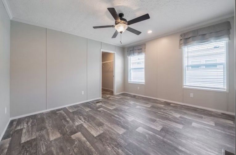 Empty bedroom with gray panel walls, wood-look flooring, ceiling fan, and two windows.