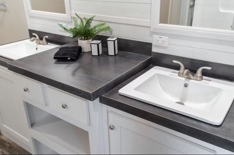 Bathroom vanity with two sinks, gray countertops, white cabinets, and mirrors.