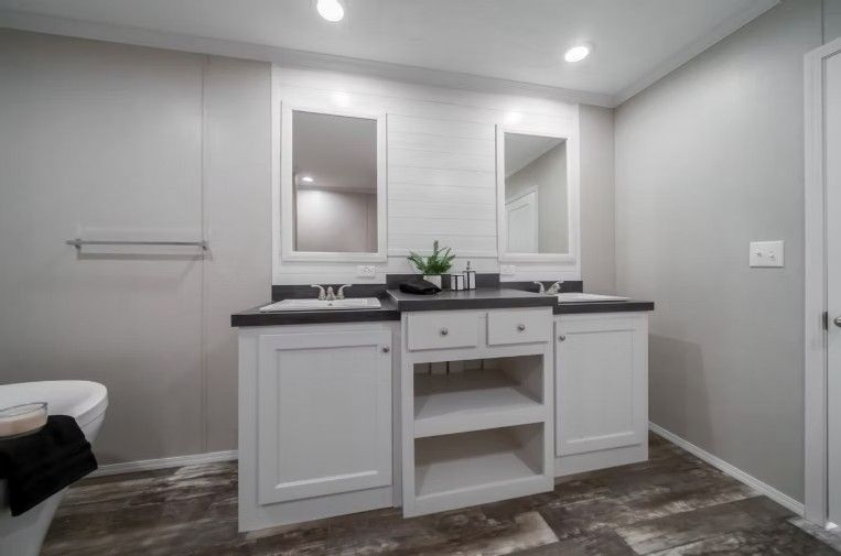 Bathroom with double vanity, white cabinets, dark countertop, and two mirrors.