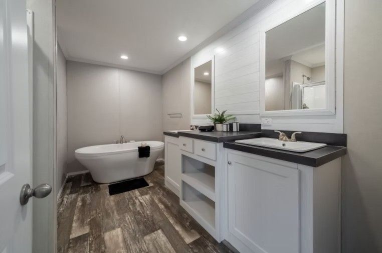 Modern bathroom with a white bathtub, double vanity with mirrors, and gray wood-look flooring.