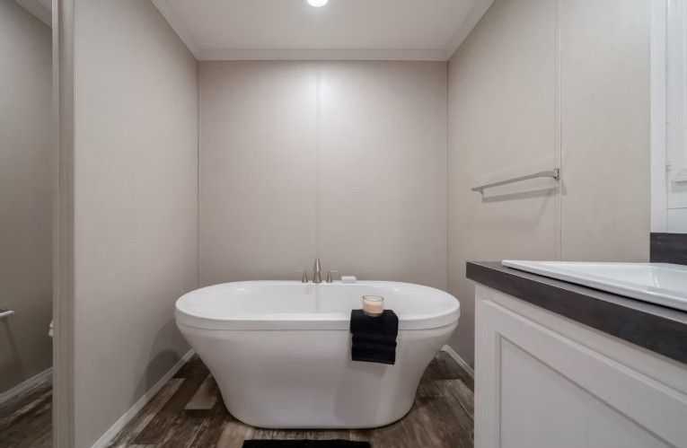 Freestanding white bathtub in a bathroom, next to a sink. Pale walls and dark floor.