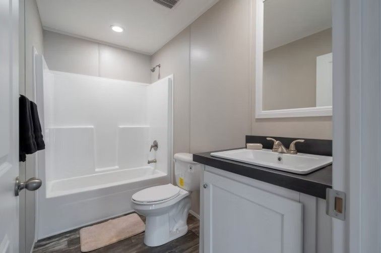 Bathroom with white tub/shower combo, toilet, sink with black countertop, and a mirror.