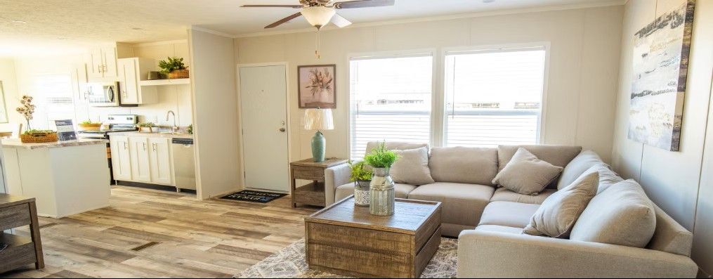 Living room with white kitchen, sectional sofa, and wood flooring.