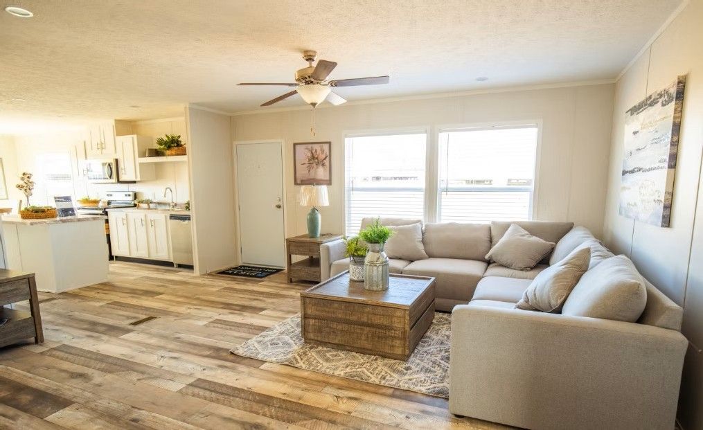 Living room with beige sectional, rustic coffee table, wood-look floor, and open kitchen.