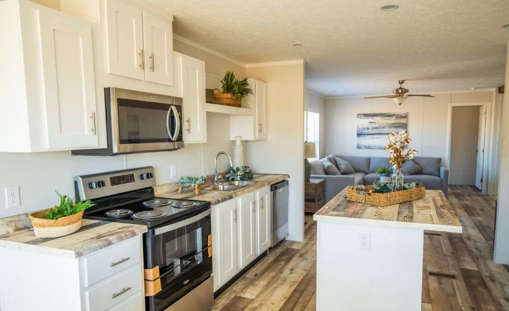White kitchen with stainless steel appliances, open to living room with gray couch.