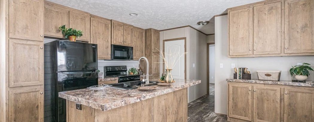 Kitchen with wood cabinets, black refrigerator, and island with countertop. Doorway in the background.