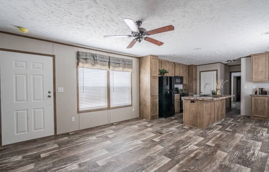 Interior view of a kitchen and living space with wood cabinets and flooring, and a ceiling fan.