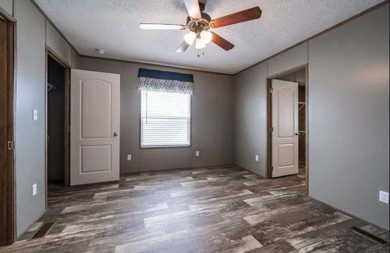 Bedroom with gray walls, wood-look floor, window, ceiling fan, and open doorways.